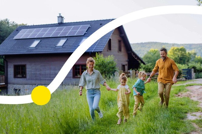 Eine Familie mit zwei Kindern läuft fröhlich vor einem Holzhaus mit Solaranlage auf dem Dach