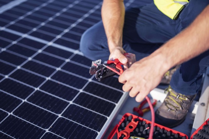 Elektriker bei der Installation von Solarmodulen auf einem Dach zur Verwertung von überschüssigem Strom